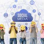 five people holding emoji face cutouts stand in front of a wall with social media icons and text