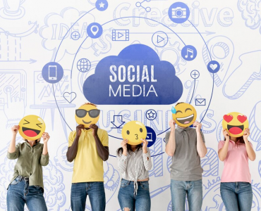 five people holding emoji face cutouts stand in front of a wall with social media icons and text